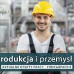 Uśmiechnięty pracownik w zakładzie przemysłowym, w kasku i odzieży roboczej.
