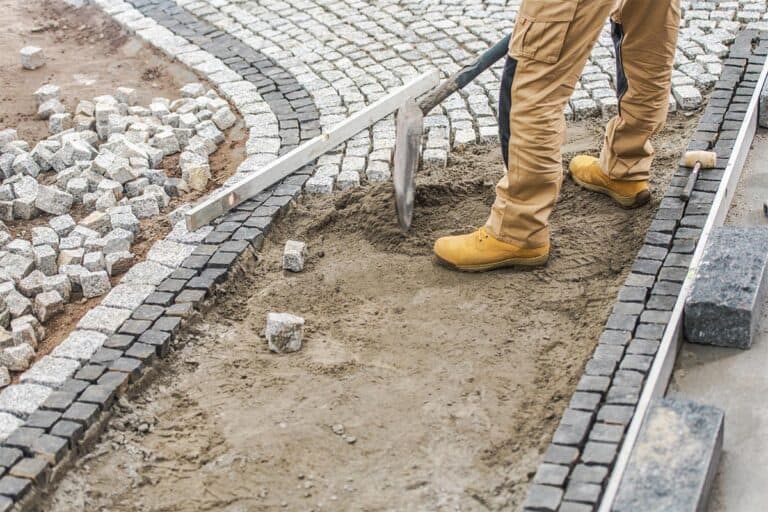 Układanie kostki brukowej w Giedlarowej - pracownik wyrównuje piasek pod szare kostki chodnikowe.