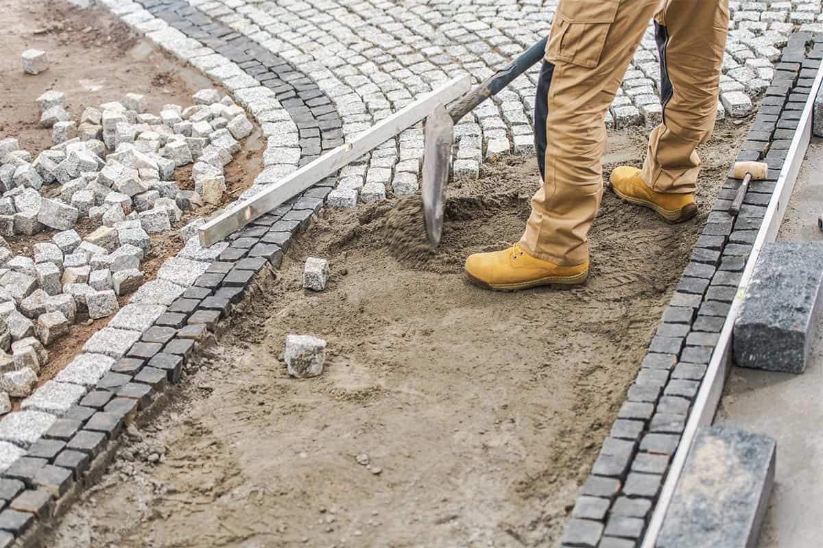 Układanie kostki brukowej w Giedlarowej - pracownik wyrównuje piasek pod szare kostki chodnikowe.